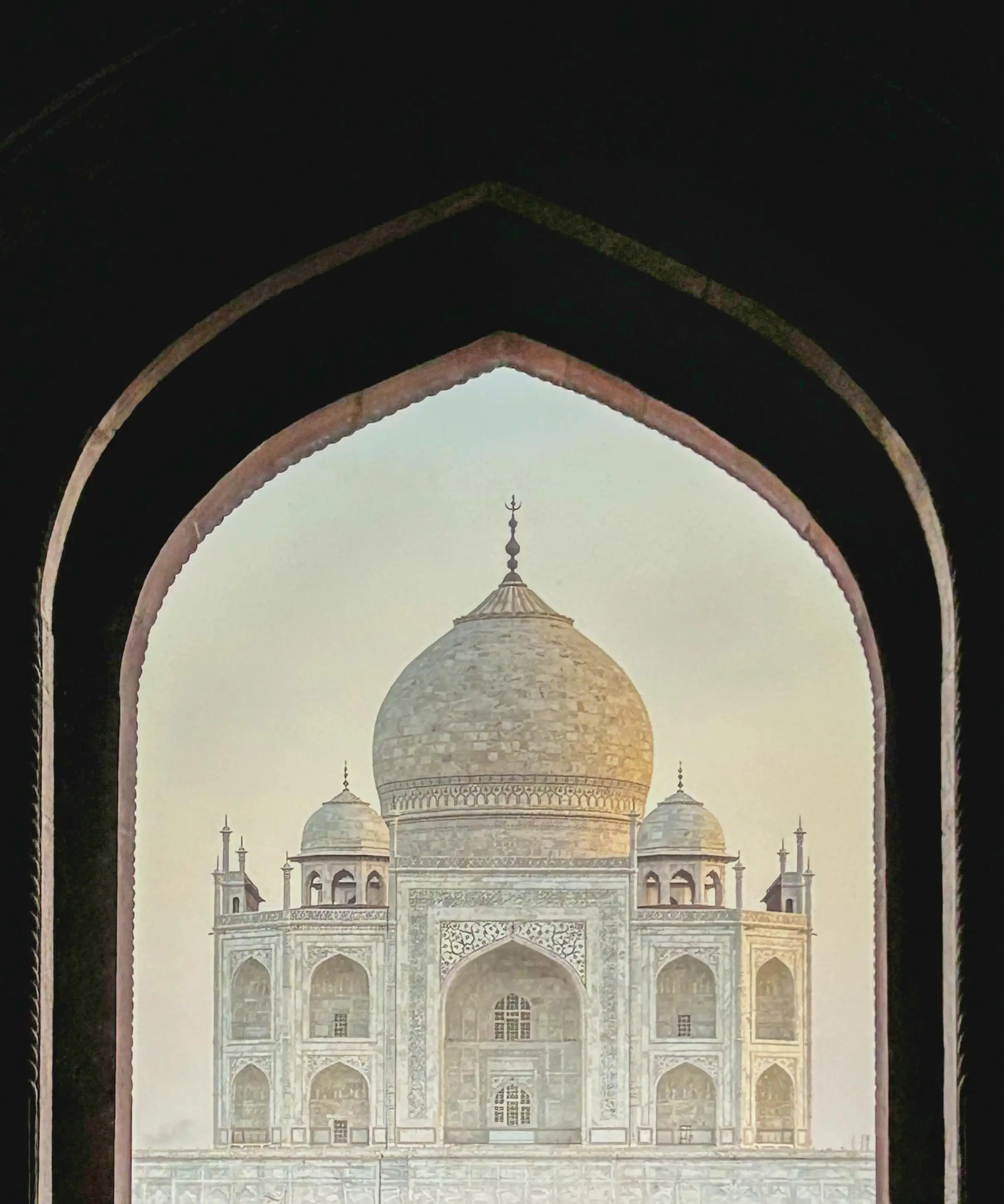 Taj Mahal at sunrise &mdash; rose-gold marble glowing through the Great Gate arch at first entry