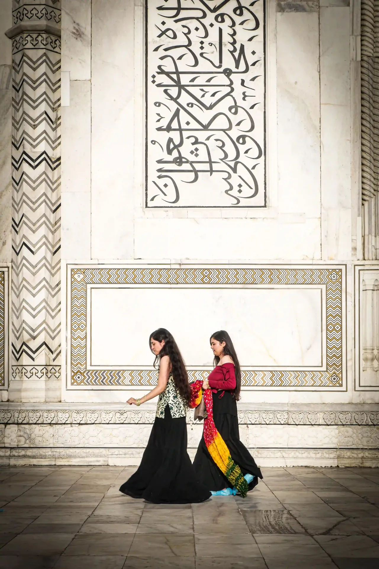 Two visitors walking past a Quranic calligraphy panel on the Taj Mahal