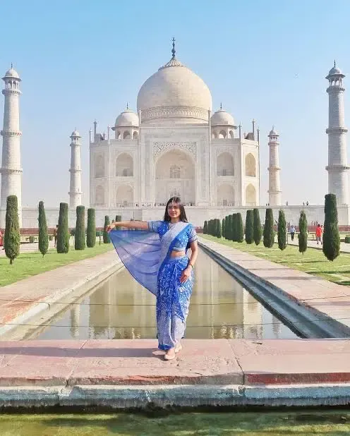 A woman in a blue saree beside the Taj Mahal reflecting pool